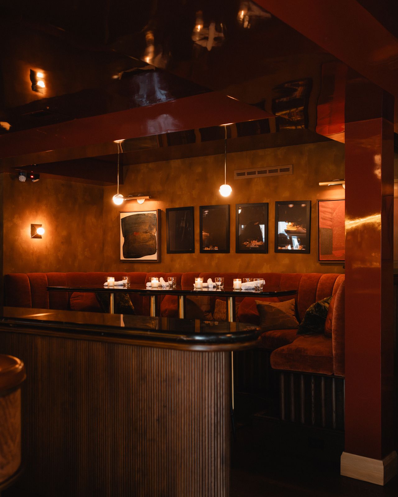 Candlelit red velvet booth beneath a wall of framed art