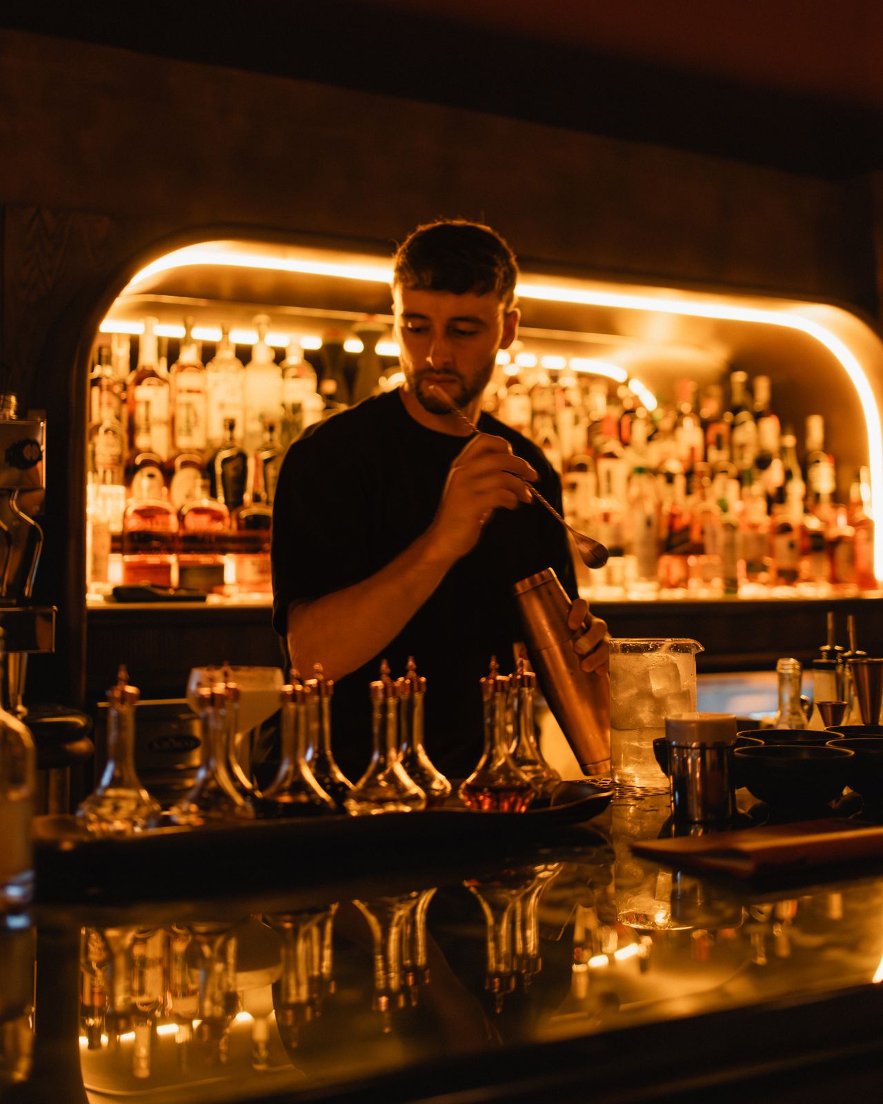 Bartender stirring a cocktail behind glowing shelves of spirits